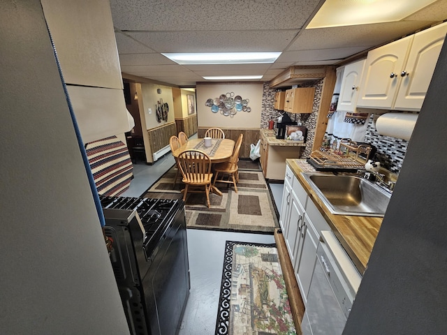 kitchen featuring a sink, a drop ceiling, white cabinetry, wainscoting, and dishwasher