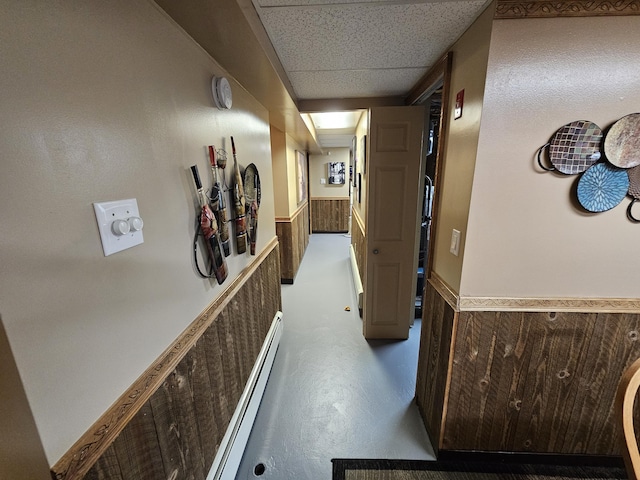 hallway with a baseboard heating unit and a wainscoted wall