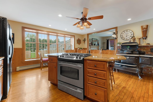 96 Grove St, Lewiston, ME 04240 - kitchen featuring gas stove, a ceiling fan, a baseboard radiator, a wainscoted wall, and freestanding refrigerator