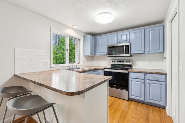 17 Graham Rd Unit 17, Westbrook, ME 04092 - kitchen featuring appliances with stainless steel finishes, a peninsula, a sink, blue cabinetry, and a textured ceiling