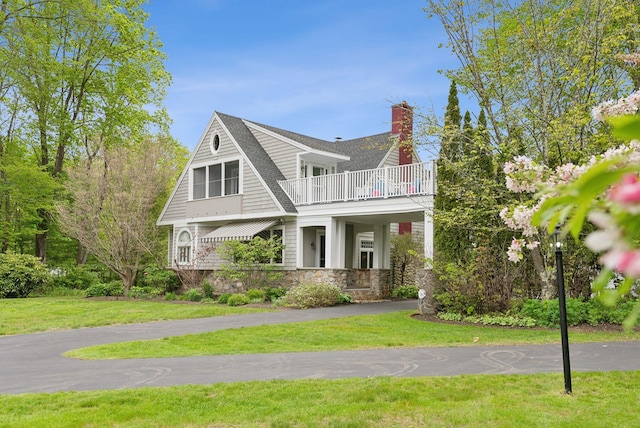 71 N St, Kennebunkport, ME 04046 - view of front of home featuring a balcony, a front lawn, a chimney, stone siding, and roof with shingles