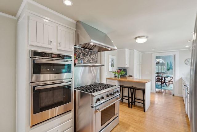 71 N St, Kennebunkport, ME 04046 - kitchen featuring wall chimney exhaust hood, appliances with stainless steel finishes, wooden counters, white cabinetry, and light wood-type flooring