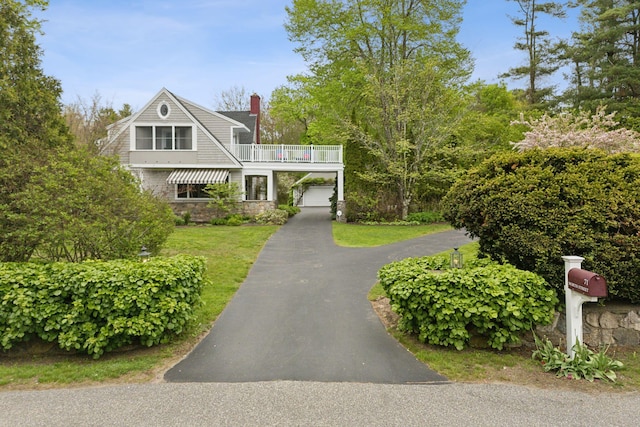 71 N St, Kennebunkport, ME 04046 - view of front of house with driveway, stone siding, a front yard, a balcony, and a chimney