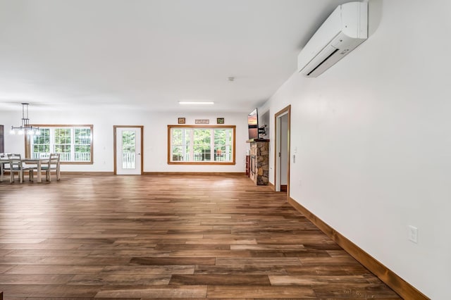 66 Mcnally Rd, Clinton, ME 04927 - unfurnished living room with a wall unit AC, dark wood-style flooring, baseboards, and a chandelier