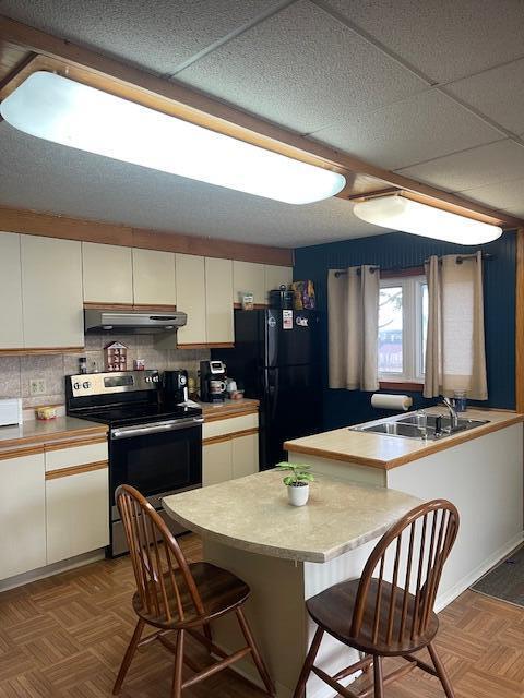 145 12th Ave, Madawaska, ME 04756 - kitchen with stainless steel electric range oven, under cabinet range hood, white cabinetry, a breakfast bar area, and a drop ceiling