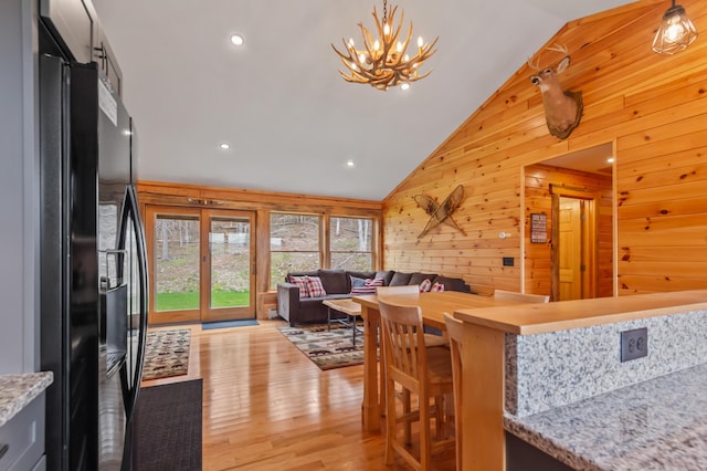 3935 Main St, Rangeley, ME 04970 - kitchen with freestanding refrigerator, lofted ceiling, wooden walls, a chandelier, and light wood-type flooring