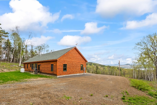 3935 Main St, Rangeley, ME 04970 - view of property exterior with dirt driveway, a shingled roof, a mountain view, faux log siding, and central AC unit
