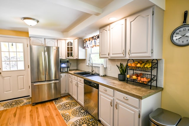 77 Carter St, Portland, ME 04103 - kitchen with stainless steel appliances, a sink, light wood-style floors, decorative backsplash, and white cabinetry