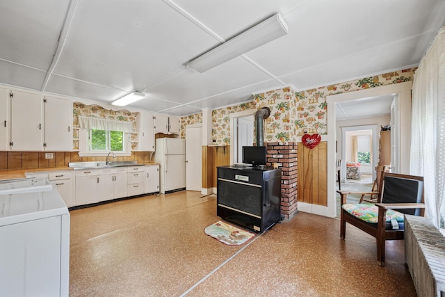 26 Unity Rd, Albion, ME 04910 - kitchen with freestanding refrigerator, wallpapered walls, a wood stove, washer / clothes dryer, and white cabinetry