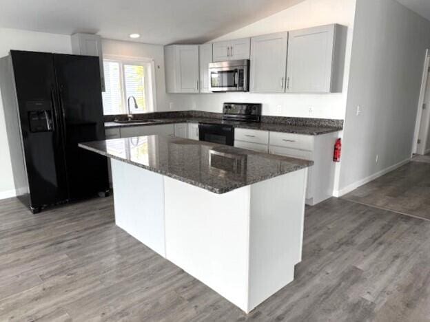 5 N Vigue Shore Rd, Albion, ME 04910 - kitchen with black appliances, a sink, dark stone counters, wood finished floors, and a center island