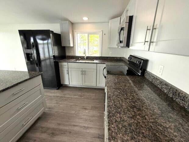5 N Vigue Shore Rd, Albion, ME 04910 - kitchen featuring a sink, black appliances, wood finished floors, dark stone counters, and white cabinets