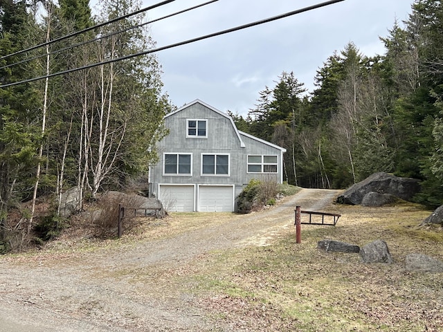 640 Bald Mountain Rd, Rangeley, ME 04970 - view of property exterior with driveway, a gambrel roof, a garage, and a view of trees