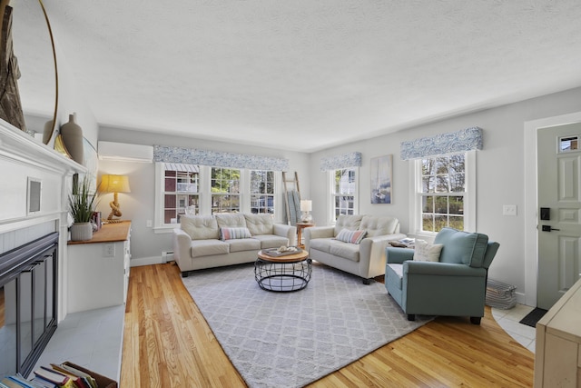 10 Lake Ave, Old Orchard Beach, ME 04064 - living area featuring a wall unit AC, a glass covered fireplace, light wood-type flooring, a textured ceiling, and baseboards