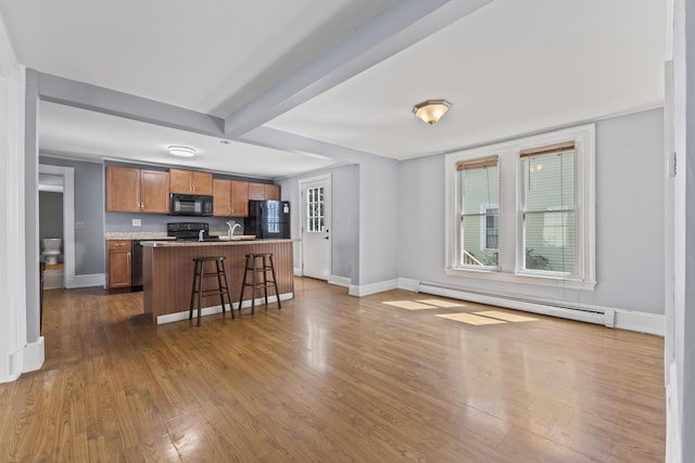 130 W Broadway, Bangor, ME 04401 - kitchen with black appliances, a baseboard heating unit, dark wood finished floors, brown cabinets, and an island with sink