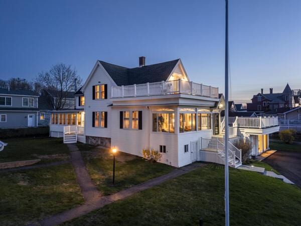 17 Bank Rd, York, ME 03909 - back of property at dusk with a balcony, stairs, a lawn, and a sunroom