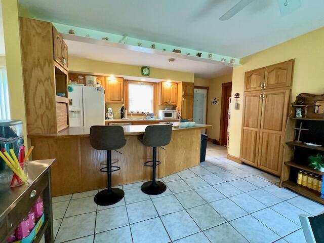 224 E Waterman Rd, Auburn, ME 04210 - kitchen featuring white refrigerator with ice dispenser, a kitchen bar, a peninsula, light countertops, and light tile patterned flooring