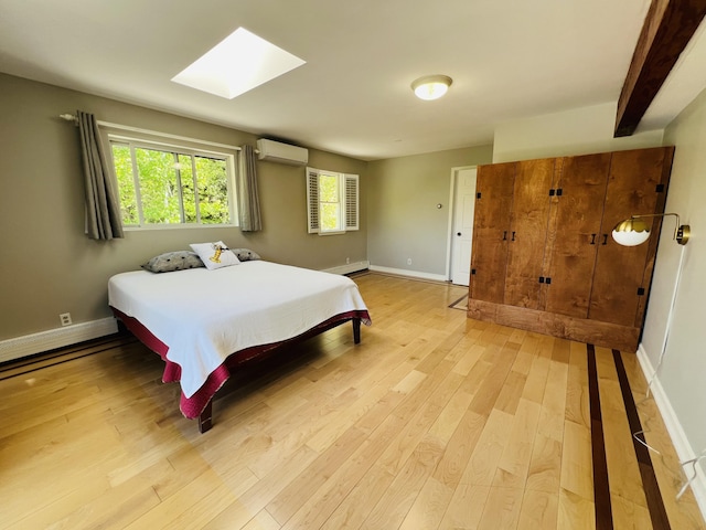 341 Ellsworth Rd, Blue Hill, ME 04614 - bedroom featuring an AC wall unit, light wood-style flooring, a skylight, and baseboards