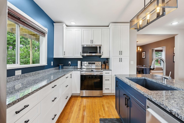 124 Dumont Ave, Lewiston, ME 04240 - kitchen with appliances with stainless steel finishes, a sink, white cabinetry, light wood finished floors, and hanging light fixtures