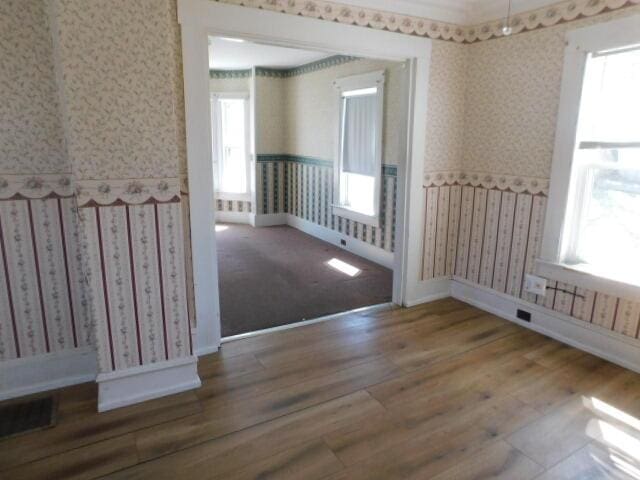 10 Summer St, Calais, ME 04619 - empty room featuring wallpapered walls, wood finished floors, healthy amount of natural light, wainscoting, and baseboards
