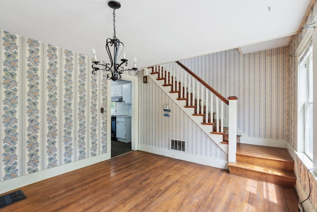 705707 Maine Ave, Farmingdale, ME 04344 - unfurnished dining area featuring wallpapered walls, hardwood / wood-style flooring, a chandelier, stairs, and baseboards