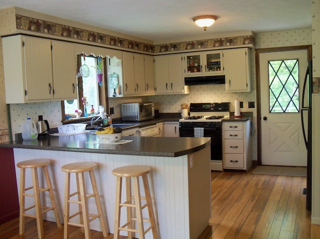 593 S Strong Rd, Strong, ME 04983 - kitchen with gas stove, under cabinet range hood, healthy amount of natural light, a peninsula, and wallpapered walls