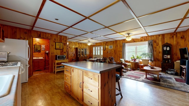 574 Scribner Hill Rd, Otisfield, ME 04270 - kitchen with stainless steel microwave, ceiling fan, wood walls, light wood-style flooring, and a center island