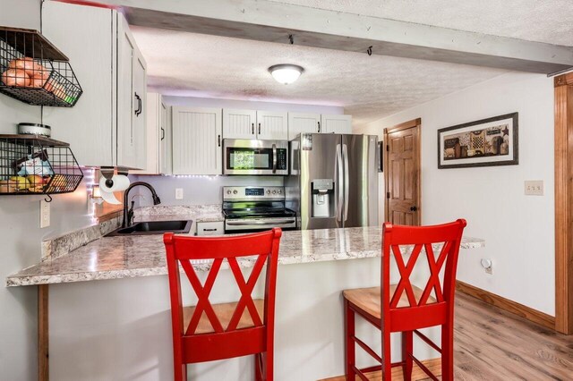6 Sand Pond Rd, North Berwick, ME 03906 - kitchen featuring stainless steel appliances, a sink, a textured ceiling, a peninsula, and light wood finished floors