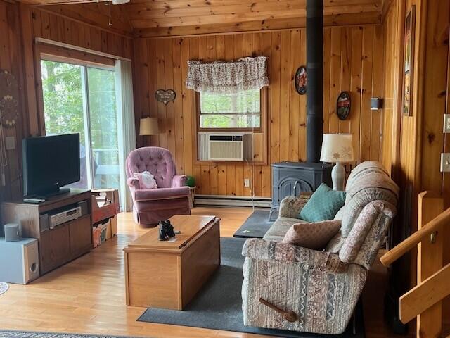 166 Ridge Rd, Frye Island, ME 04071 - sitting room featuring baseboard heating, a wood stove, light wood finished floors, wood walls, and cooling unit