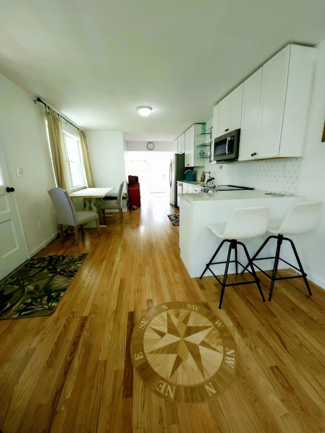 567 Ossipee Trl W, Standish, ME 04084 - kitchen featuring appliances with stainless steel finishes, white cabinetry, light wood-style floors, a peninsula, and backsplash