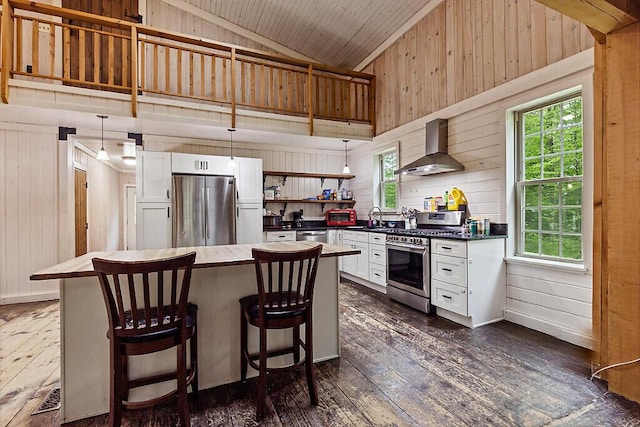 16 Trillium Ests, Rome, ME 04963 - kitchen with wall chimney range hood, appliances with stainless steel finishes, wood walls, dark wood finished floors, and white cabinets