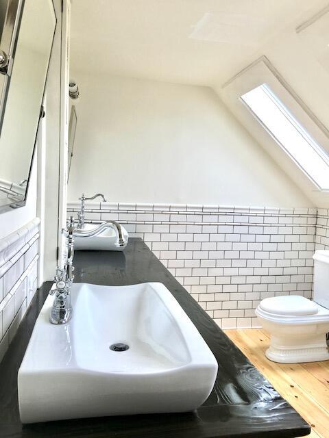 1 Forest St, Dover-Foxcroft, ME 04426 - bathroom featuring tile walls, a sink, toilet, a skylight, and vaulted ceiling