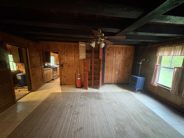 15 Sawyer Ln, Sanford, ME 04083 - unfurnished living room featuring a wood stove, wooden walls, ceiling fan, beam ceiling, and light floors