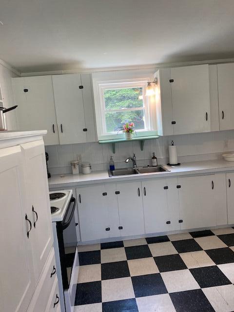 58 Main St, Sangerville, ME 04479 - kitchen featuring range, light flooring, a sink, decorative backsplash, and white cabinetry