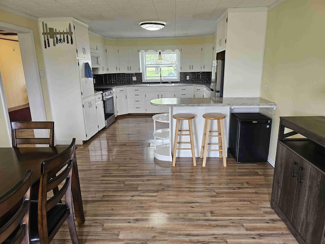393 Main St, Limestone, ME 04750 - kitchen featuring appliances with stainless steel finishes, a peninsula, dark wood finished floors, tasteful backsplash, and white cabinets