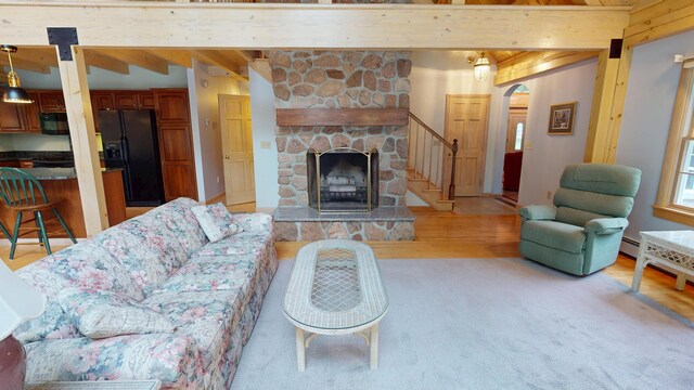129 Maple Shore Ln, Stetson, ME 04488 - living room featuring light wood-style flooring, beam ceiling, arched walkways, a stone fireplace, and stairway