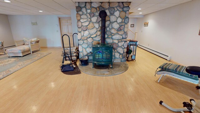 129 Maple Shore Ln, Stetson, ME 04488 - living room featuring baseboard heating, a paneled ceiling, a wood stove, wood finished floors, and baseboards
