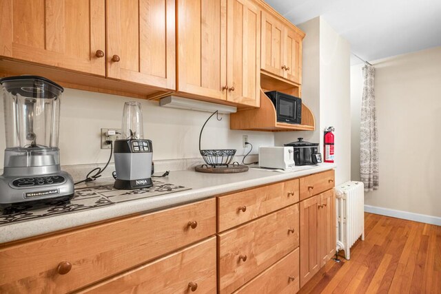 6 Winter St, Augusta, ME 04330 - kitchen featuring radiator heating unit, light countertops, light wood-style floors, light brown cabinetry, and black microwave