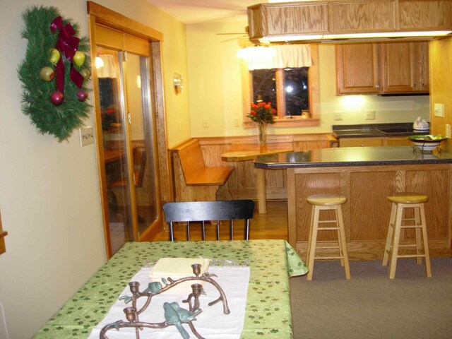 35 Viking Village Rd, Newry, ME 04261 - kitchen with brown cabinetry, a breakfast bar area, dark countertops, a peninsula, and a wainscoted wall