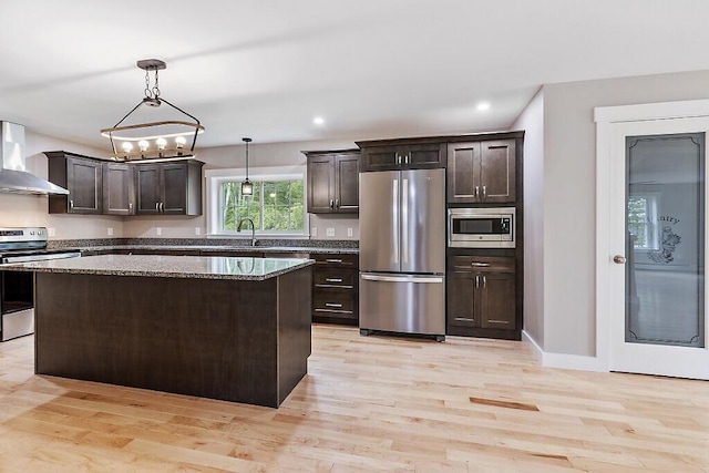 65 May Way, Sidney, ME 04330 - kitchen featuring stainless steel appliances, wall chimney range hood, dark brown cabinetry, light wood-type flooring, and a center island