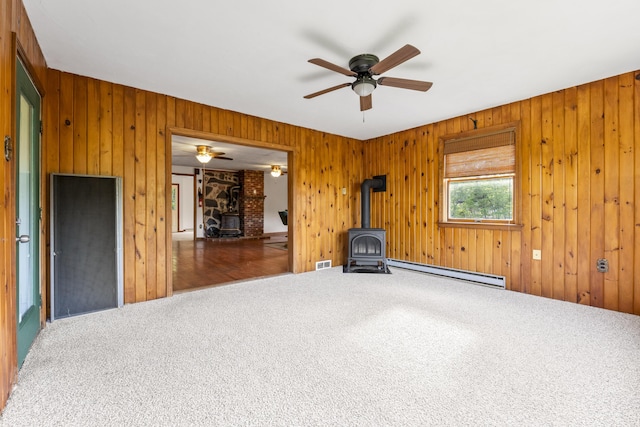 117 Taylor Woods Rd, Belgrade, ME 04917 - carpeted spare room featuring a wood stove, a baseboard heating unit, a ceiling fan, and wood walls
