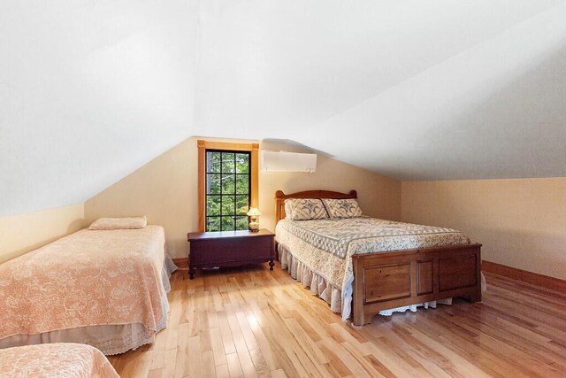 59 Lupine Dr, Belgrade, ME 04917 - bedroom featuring light wood finished floors, vaulted ceiling, a wall unit AC, and baseboards
