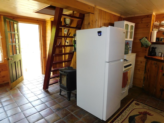 51 Pond Rd, Abbot, ME 04406 - kitchen with white appliances, wooden walls, a wood stove, white cabinetry, and dark tile patterned flooring