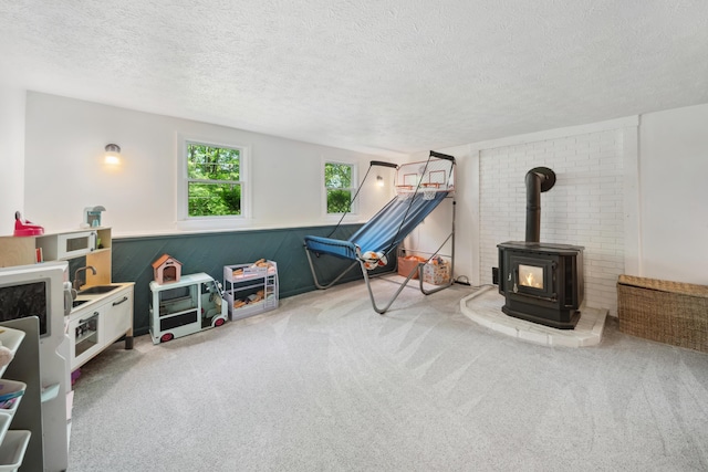 3 Wilson Ln, Saco, ME 04072 - playroom featuring carpet flooring, a wood stove, a textured ceiling, and a wainscoted wall