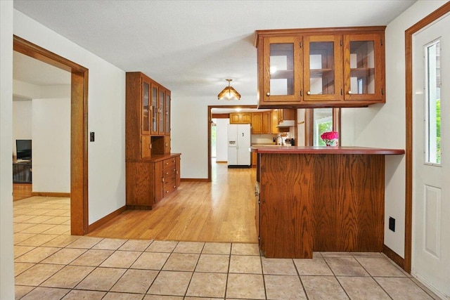 473 Davenport Hill Rd, Jay, ME 04239 - kitchen featuring white fridge with ice dispenser, brown cabinetry, light tile patterned floors, glass insert cabinets, and baseboards