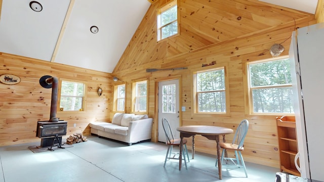 121 Loop Rd, Lincoln, ME 04457 - dining room featuring wooden walls, a wood stove, finished concrete flooring, and high vaulted ceiling