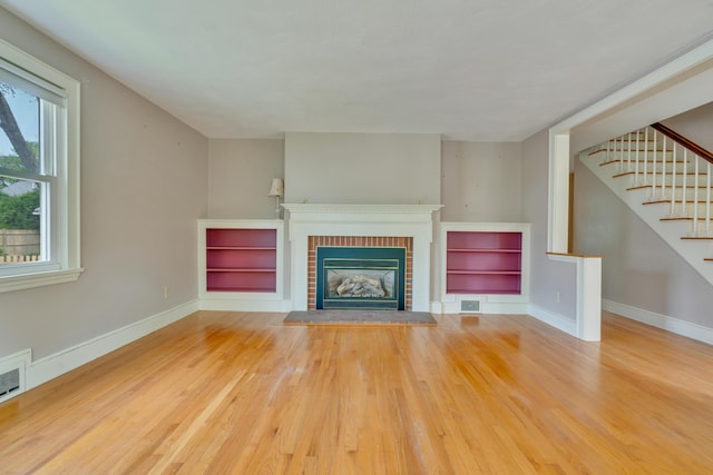 61 Carlyle Rd, Portland, ME 04103 - unfurnished living room with wood finished floors, a brick fireplace, baseboards, and stairs