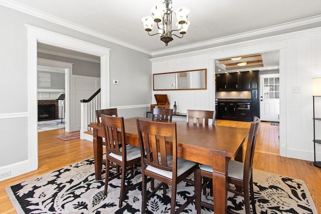 797 Main St, South Portland, ME 04106 - dining area featuring light wood finished floors, a chandelier, crown molding, a brick fireplace, and stairs
