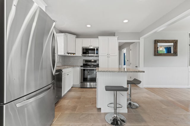 27 Seaside Ave, Saco, ME 04072 - kitchen featuring stainless steel appliances, a kitchen bar, white cabinets, a center island, and a wainscoted wall