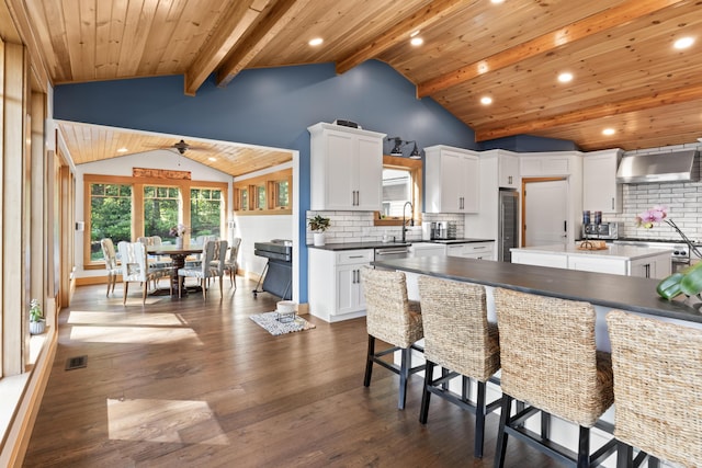 134 Zakelo Rd, Harrison, ME 04040 - kitchen featuring wall chimney range hood, dark wood-style floors, decorative backsplash, a breakfast bar area, and wooden ceiling