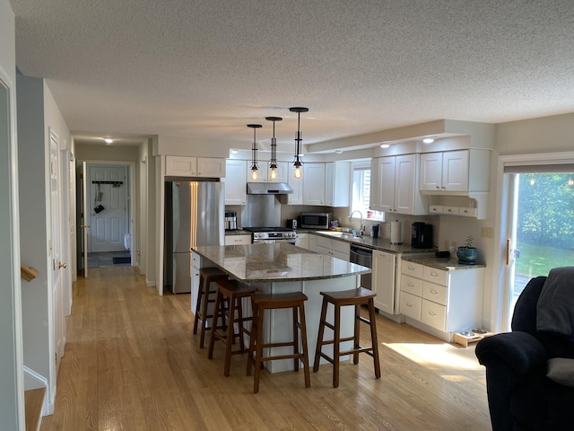 12 Cromwell Dr, Orono, ME 04473 - kitchen with stainless steel appliances, under cabinet range hood, light wood-style floors, a textured ceiling, and white cabinetry